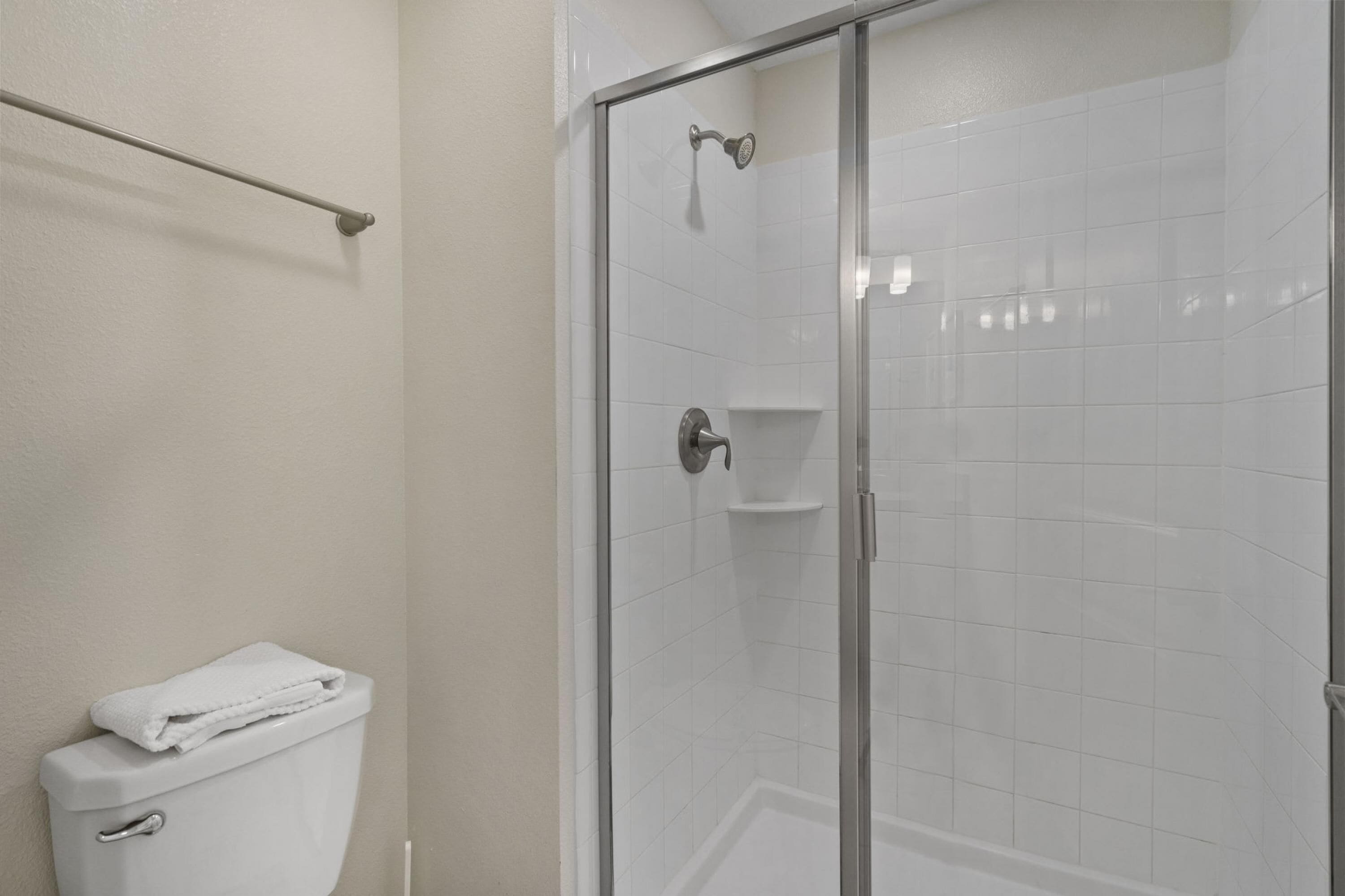 A bathroom with a glass-enclosed shower, a toilet, and a towel rack.