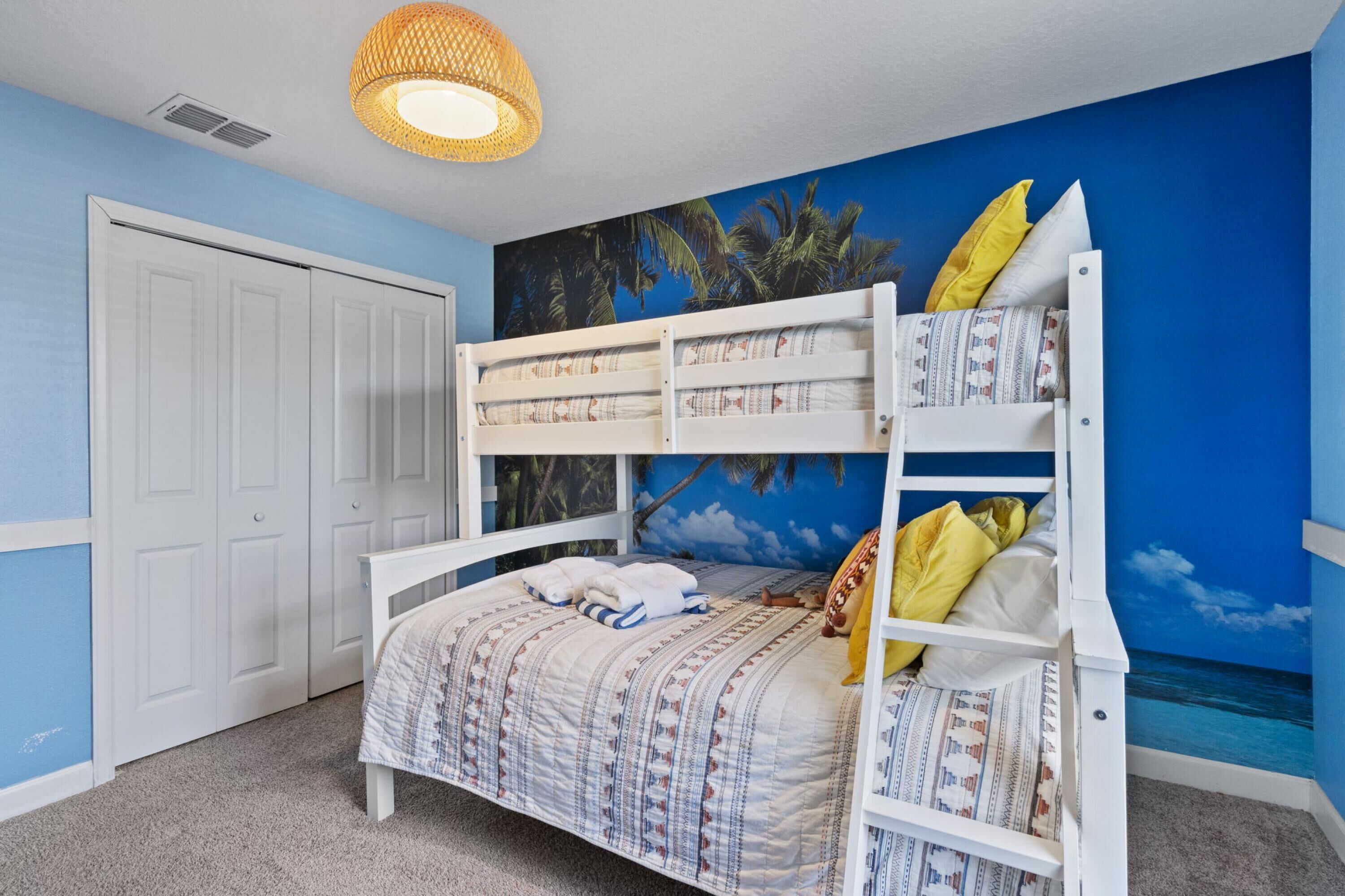 A bunk bed with a patterned bedspread and pillows, a white wardrobe, and a mural of a beach scene.