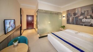 A hotel room with a bed, a TV, a glass-enclosed shower, and a cityscape painting on the wall.