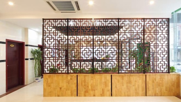 A reception area with a wooden reception desk, a decorative screen with geometric patterns, and potted plants.