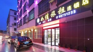 A hotel with a neon sign, a car parked in front, and a wet street.