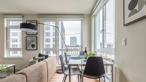 A modern apartment with a dining area, large windows, and a view of the city. - 2BR | Gym, Views | Bellevue | Sophari Parkside F (Bellevue)