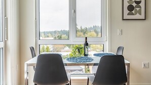 A dining area with a table, chairs, a bottle, and a framed artwork on the wall. - 2BR | Gym, Views | Bellevue | Sophari Parkside F (Bellevue)