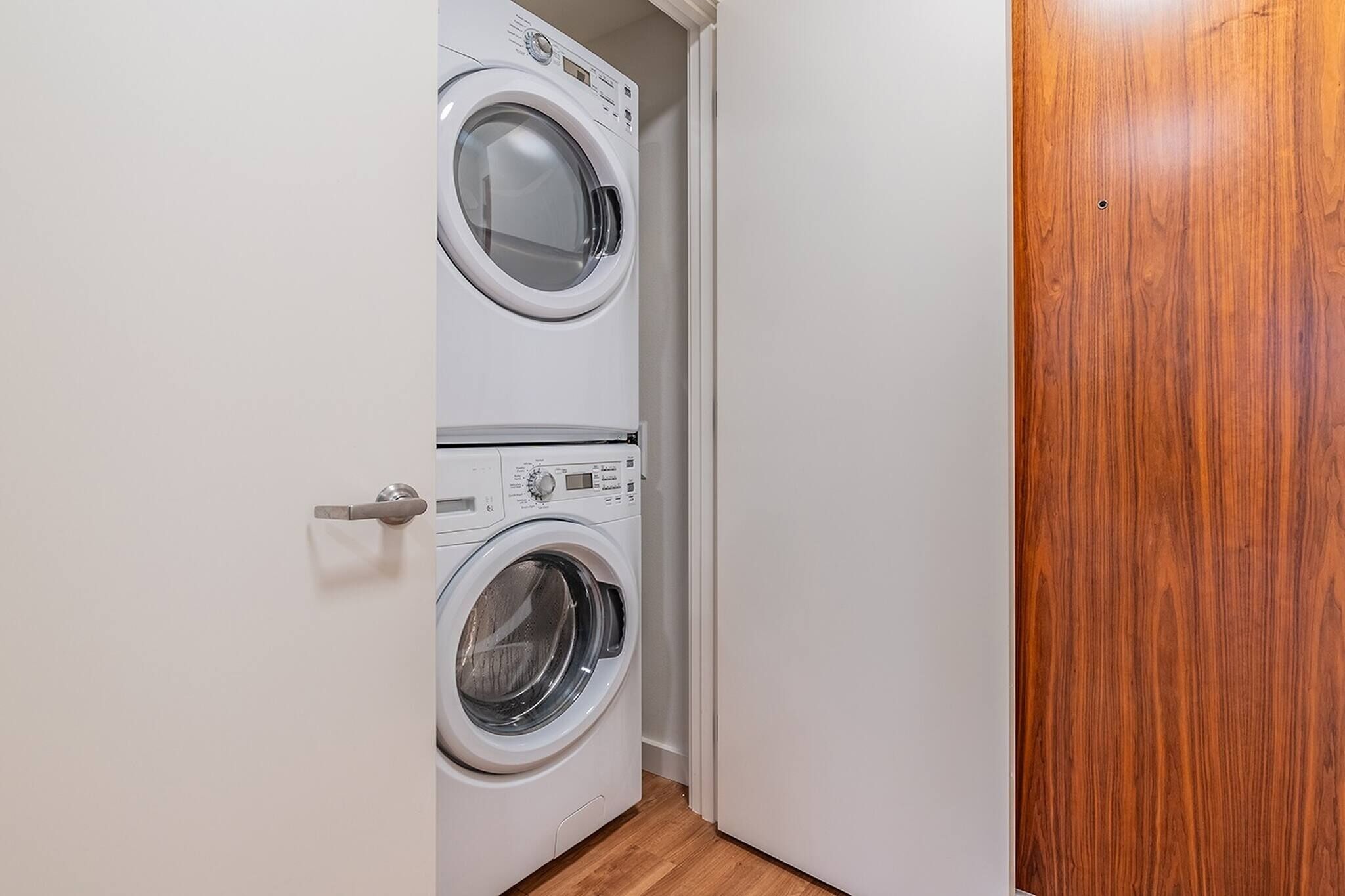 A laundry room with two stacked washing machines and a wooden door.