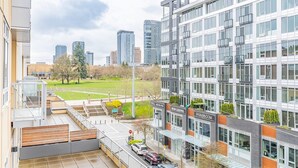 A modern building with a glass facade, a parking area, and a view of a park and cityscape. - 2BR | Gym, Views | Bellevue | Sophari Parkside F (Bellevue)
