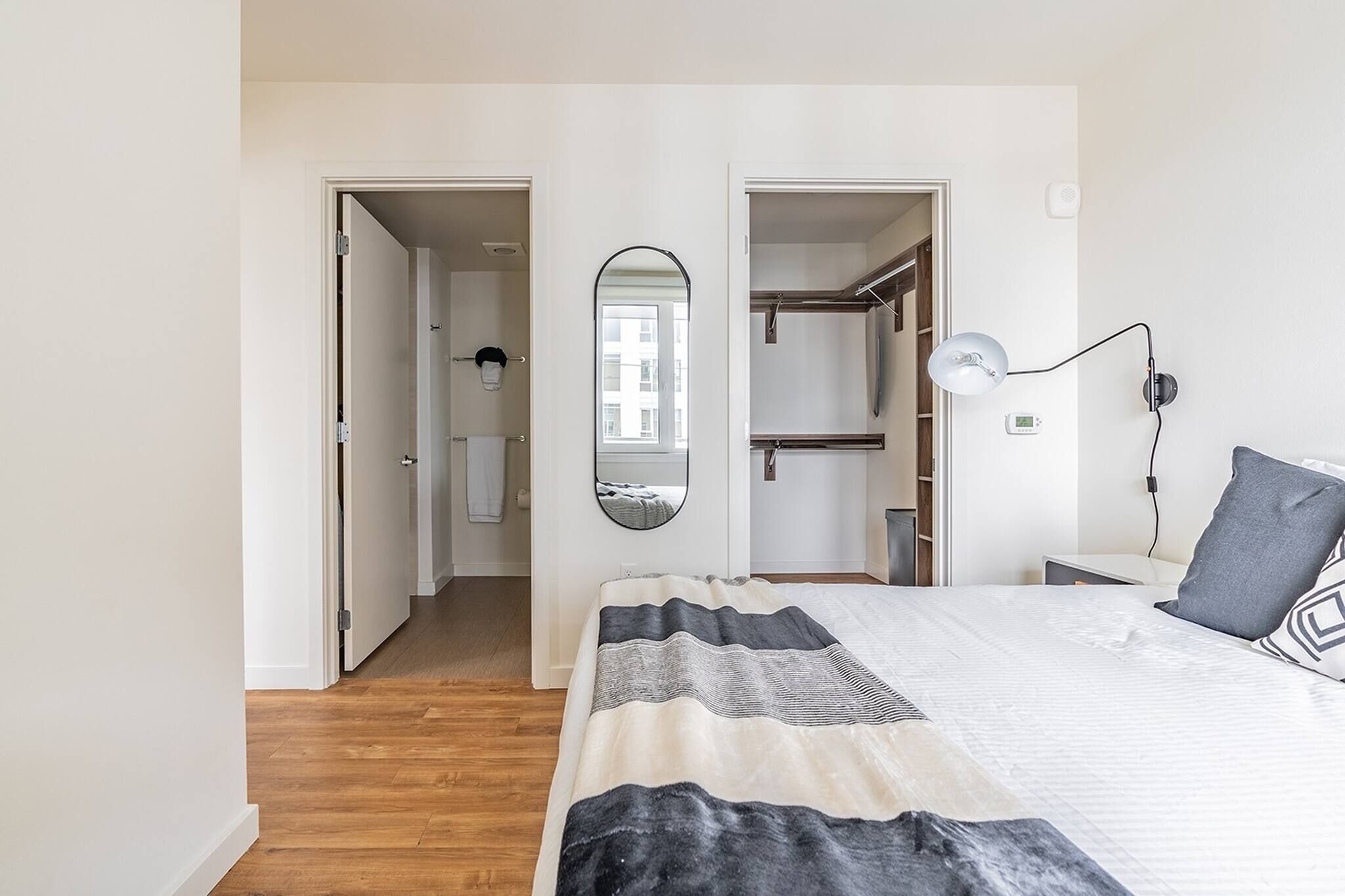 Et soveværelse med seng, sengetøj, lampe, spejl og et garderobeskab.