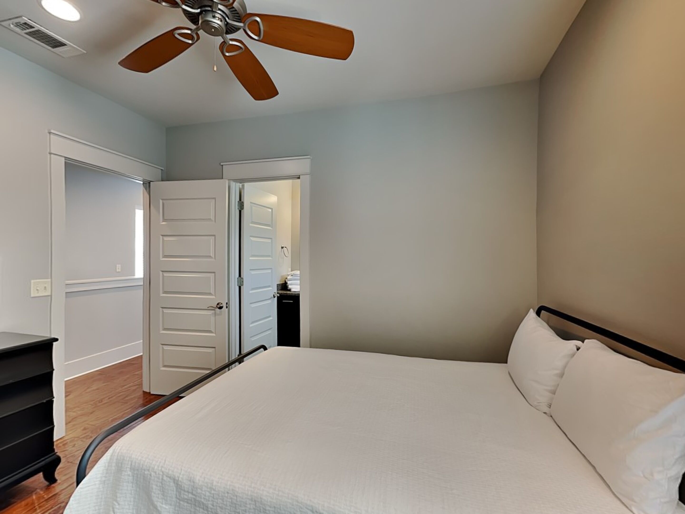 Une chambre à coucher avec un lit, un ventilateur de plafond et une porte donnant sur une salle de bain.