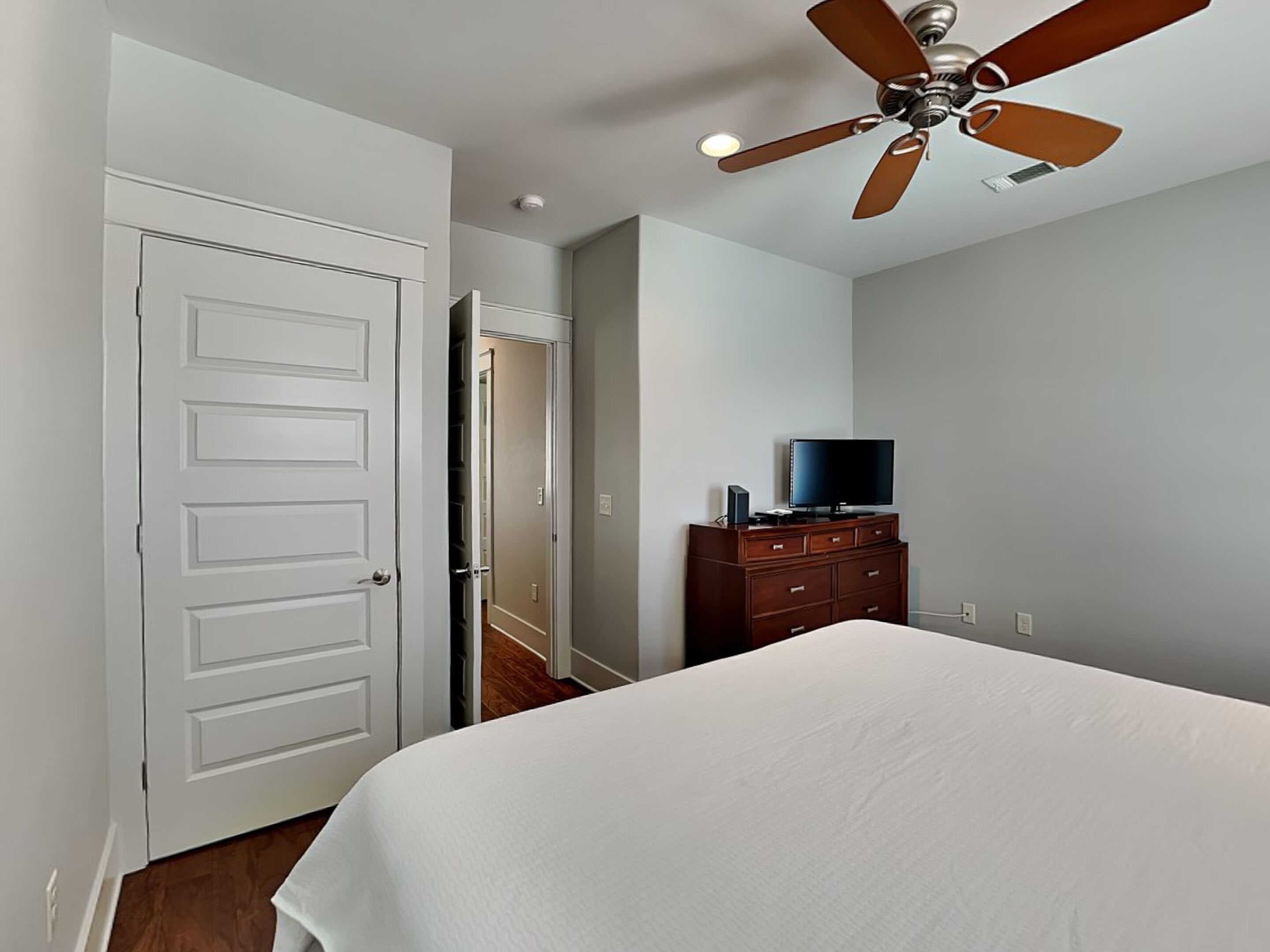 Une chambre à coucher avec un lit, un ventilateur de plafond, une commode et un téléviseur.