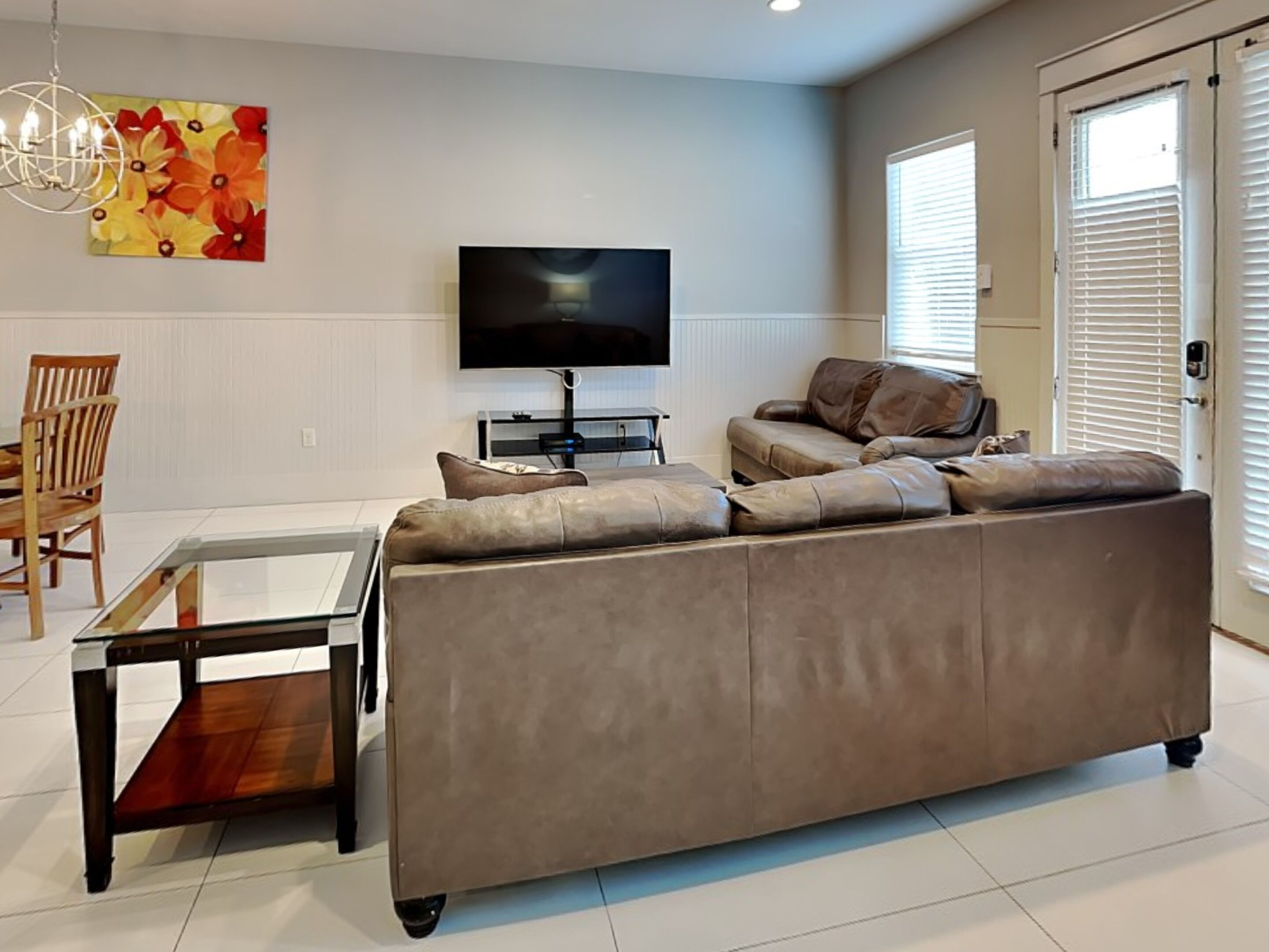 A modern living room with a leather sofa, a glass coffee table, a flat-screen TV, and a dining area with a wooden table and chairs.