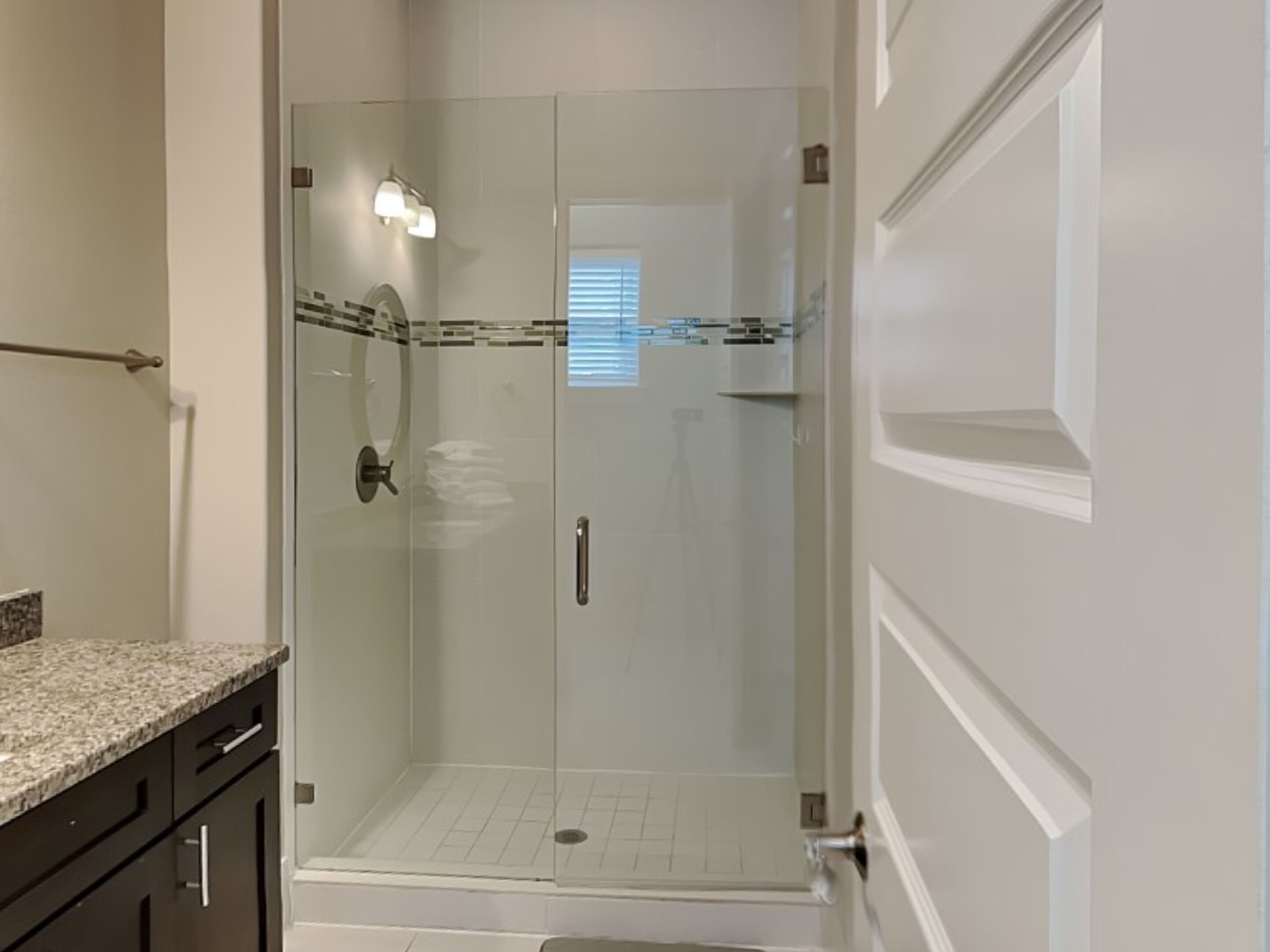 A modern bathroom with a glass-enclosed shower, a granite countertop, and dark cabinetry.