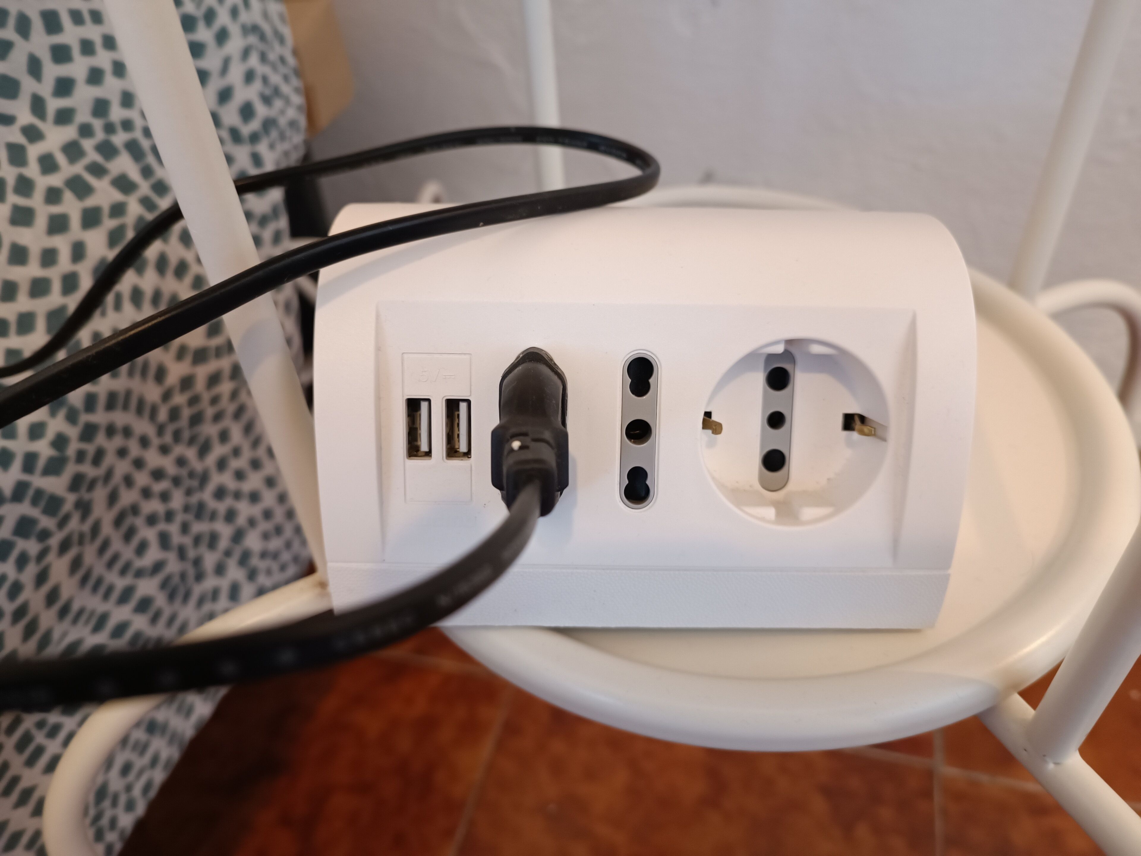 Un enchufe blanco con dos puertos USB y un clavija de tres puntas sobre una silla blanca.
