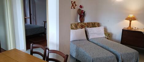 A room with two beds, a wooden table, and a lamp.