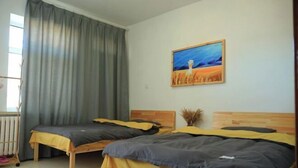 A room with two beds, a radiator, a window with curtains, and a painting on the wall.