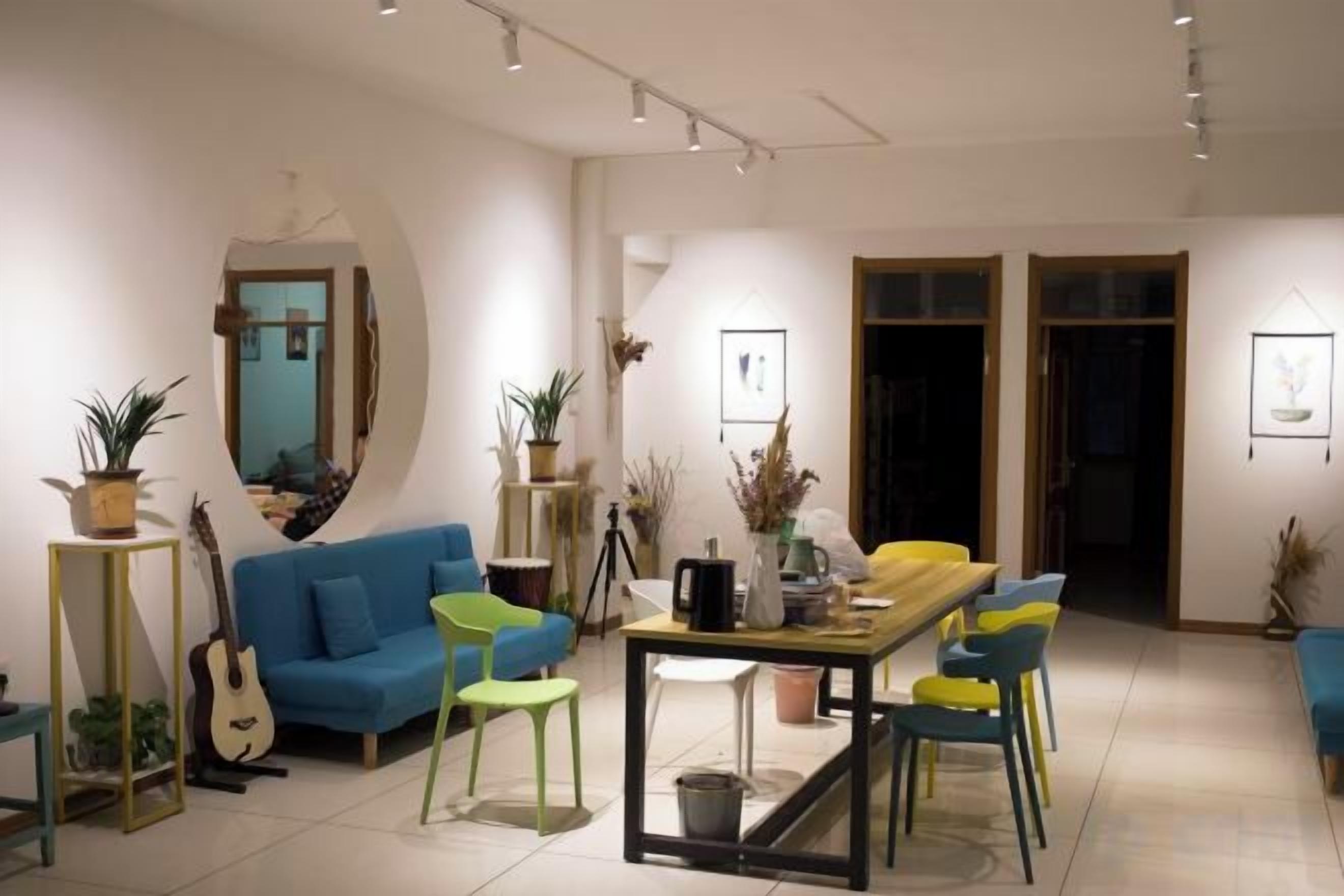 Una sala moderna con un sofá azul, una mesa de comedor amarilla y sillas verdes. Hay plantas en macetas y una guitarra en el espacio.