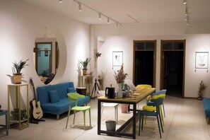 A modern living room with a blue sofa, a yellow dining table, and green chairs. There are potted plants and a guitar in the space. - Fuyuan Dongshijie Youth Hostel (Fuyuan)