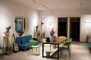 A modern living room with a blue sofa, a yellow dining table, and green chairs. There are potted plants and a guitar in the space.