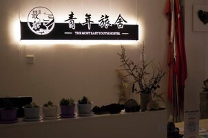 Una recepción con un letrero que dice 'THE MOST EAST YOUTH HOSTEL' y una fila de macetas con plantas al frente.