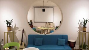 A room with a blue sofa, a round mirror, a guitar, and a drum.