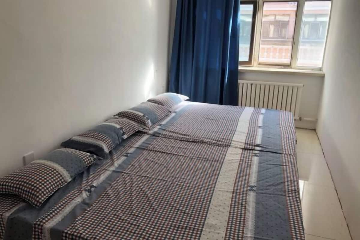 Ein Einzelbett mit gestreifter Bettwäsche, ein Fenster mit blauen Vorhängen und eine Heizung.