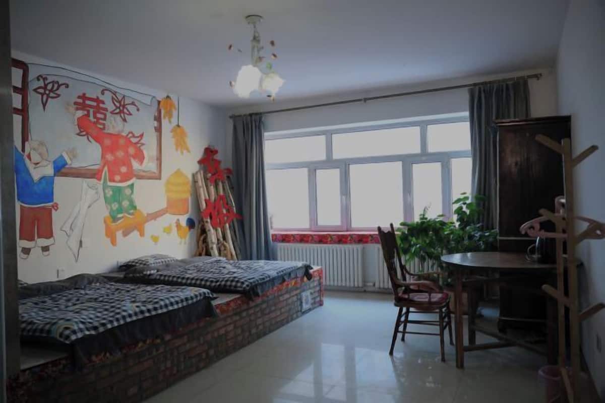 Ein Zimmer mit einem Bett, einem Schreibtisch, einem Stuhl, einem Fenster und einer Wand mit Wandgemälde.