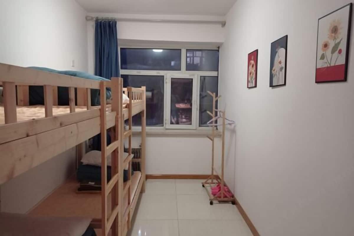Ein Zimmer mit einem Etagenbett, einem Vorhangfenster, einer Holzleiter und einem an der Wand befestigten Ablage.