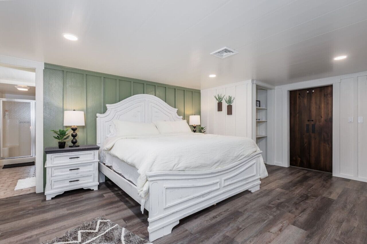 Une chambre avec un lit blanc, une table de chevet avec une lampe, une armoire en bois et un panneau mural vert.