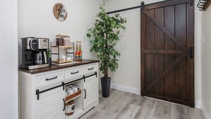 Een keuken met een koffiezetapparaat, planken met potten, een potplant en een houten deur.