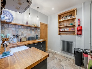 Una cocina con encimera de madera, luces colgantes, salpicadero de azulejos y un estante de madera con utensilios de cocina.
