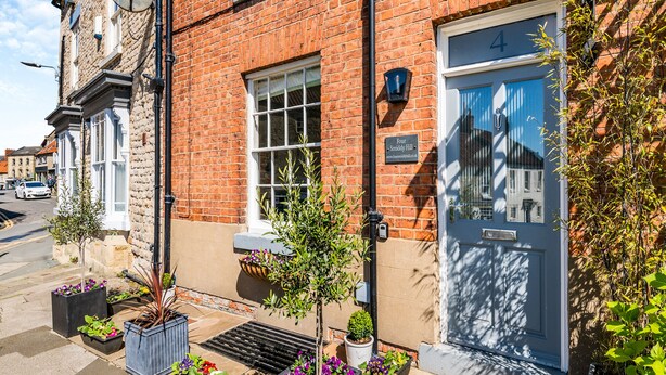 A red brick building with a white door labeled '4', a satellite dish, and potted plants.