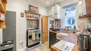 A kitchen with a gas stove, hanging pots, a tiled backsplash, and a window with a view.