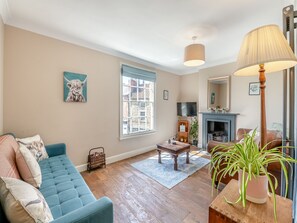 Een woonkamer met een bank, een salontafel, een lamp, een open haard en een raam.