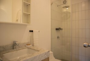 Un baño con lavamanos de mármol, cabina de ducha de vidrio y una toalla blanca colgada en la pared.