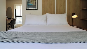 Habitación de hotel con una cama grande, un escritorio con silla, un cuadro en la pared y una lámpara de noche.