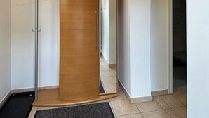 Un couloir avec une porte en bois, un étagère en métal et un tapis noir.