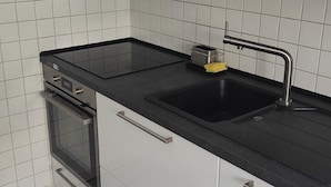 Une cuisine dotée d’un plan de travail noir, d’un évier en acier inoxydable et d’un four encastré.