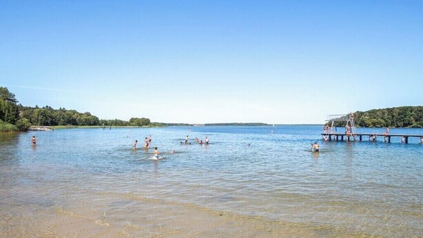 Une plage à l’eau claire, une jetée et des gens qui se baignent.