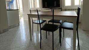 A dining area with a table and chairs, a television, and a kitchen in the background. - Fairmont Residence Alice by Ca-sa Check (Chioggia)