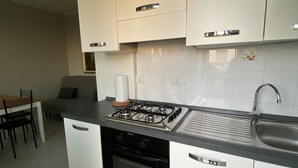 A modern kitchen with white cabinets, a gas stove, a sink, and a dining area with a table and chairs. - Fairmont Residence Alice by Ca-sa Check (Chioggia)