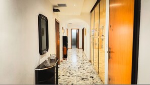Um corredor de hotel com piso de mármore, portas de madeira e um espelho na parede.