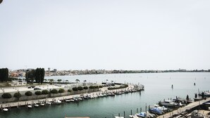 Uma marina com barcos atracados, um calçadão à beira-mar e um horizonte urbano ao longe.