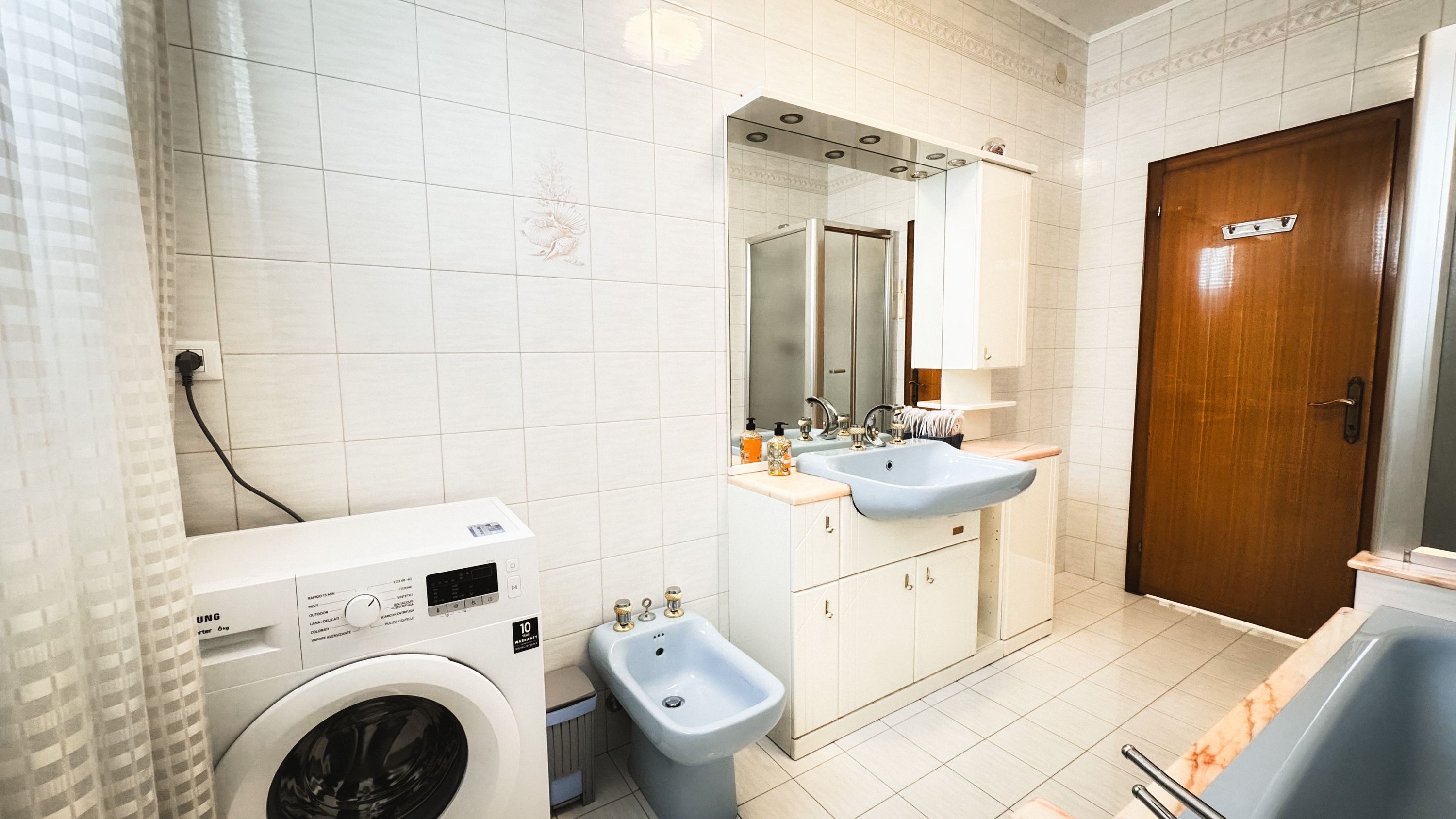 A modern bathroom with a washing machine, bidet, sink, and mirror.
