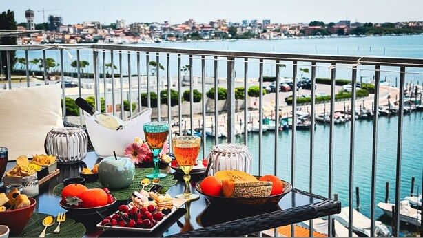 Varanda com mesa posta para o café da manhã, com vista para um porto e paisagem urbana.