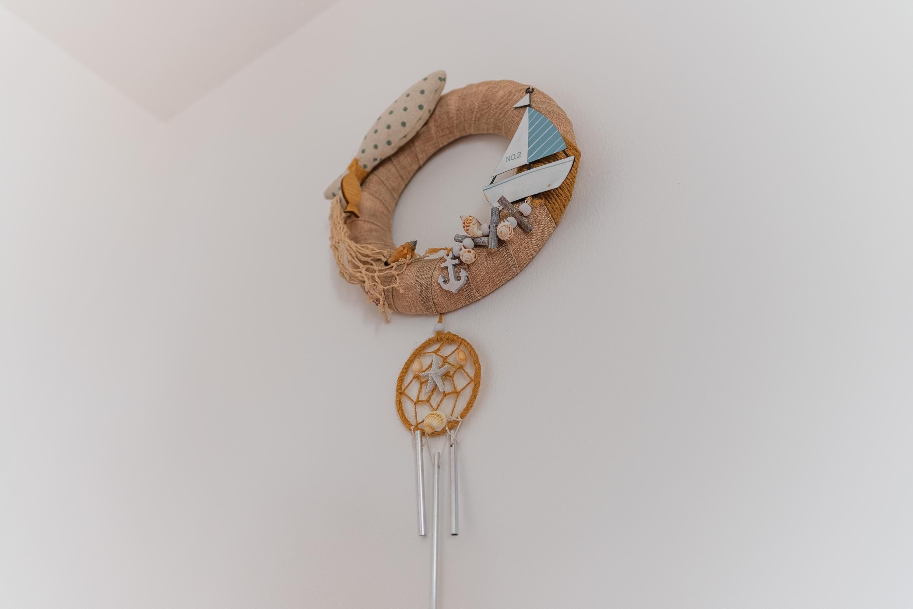 A wall-mounted decorative wreath with a sailboat and anchor, and a dreamcatcher below it.