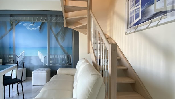 A modern living room with a white sofa, a wooden staircase, and a view of the ocean through a glass door. - Fairmont Residence Elisabetta by Ca-sa Check (Chioggia)