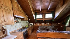 Een knus kamer in blokhutstijl met houten vloeren, een kitchenette, een bed met beddengoed met dessin en een eethoek.