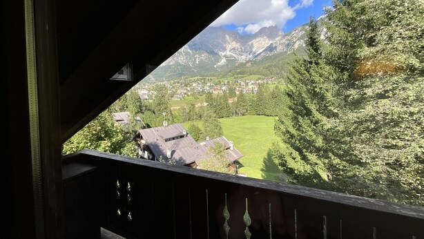 Een balkon met uitzicht op een berglandschap, inclusief huizen en begroeiing.