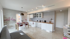 Una cocina moderna con armarios blancos, un comedor con una mesa dispuesta para dos personas y un mural de flamencos en la pared.
