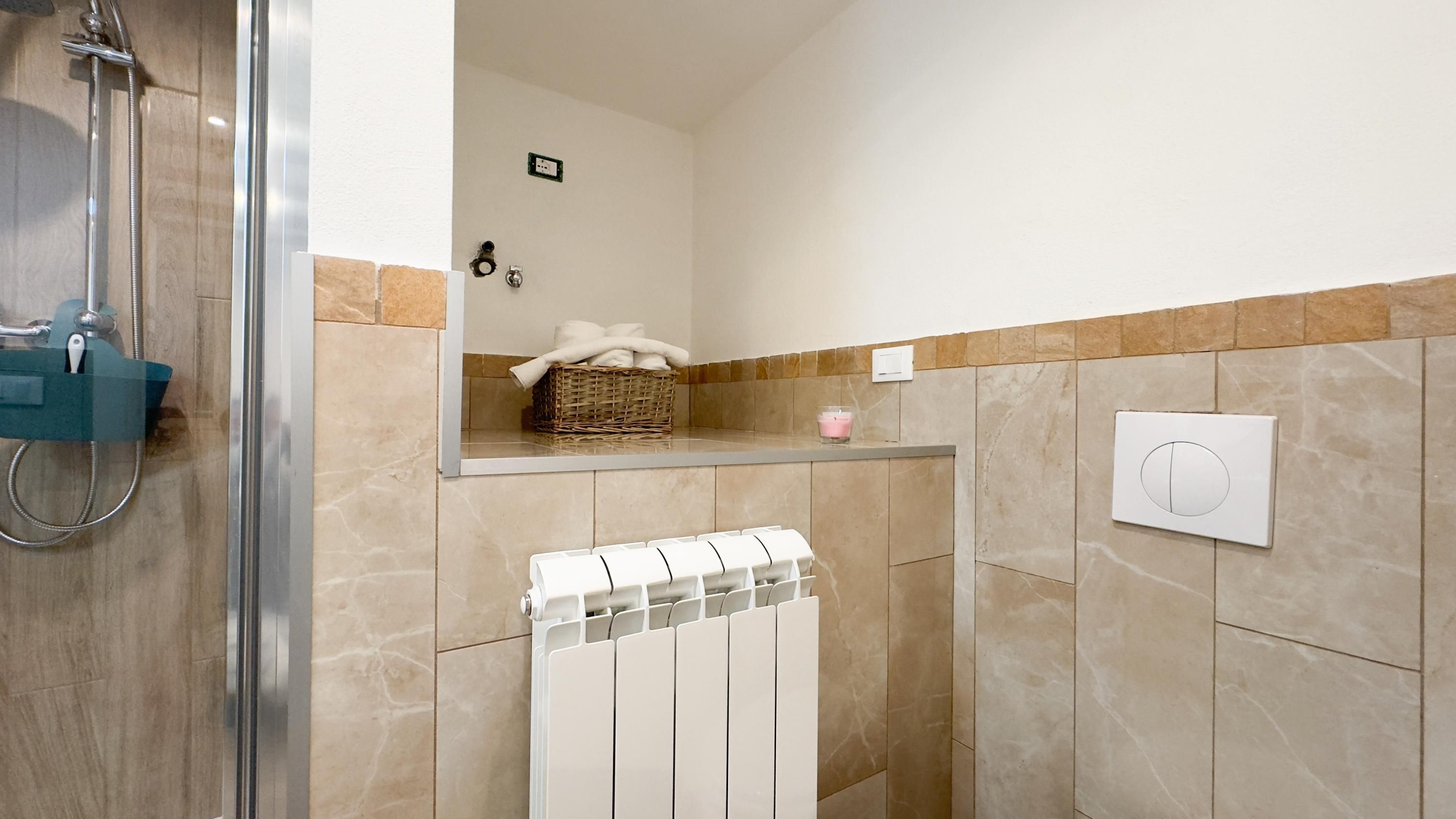 Une salle de bain avec une douche à parois de verre, un porte-serviettes blanc, un thermostat fixé au mur et un panier en osier contenant des serviettes.