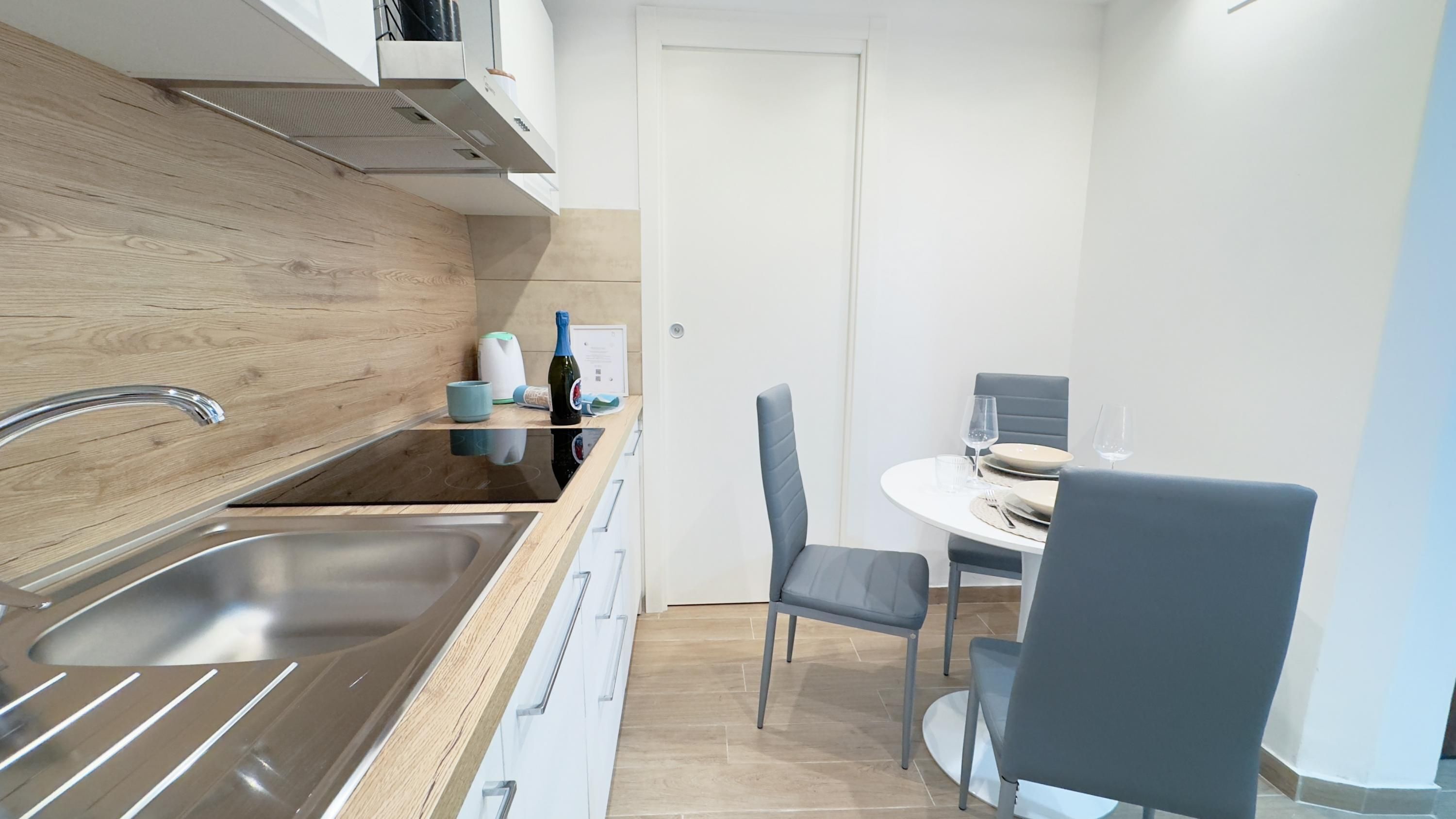 A compact kitchen with a stainless steel sink, a built-in oven, and a small dining area with a round table and two chairs.
