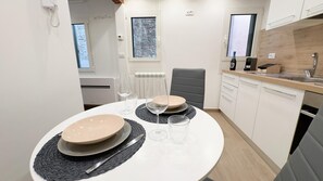 Et moderne køkken med hvide skabe, en træbordplade og et spiseområde med et rundt bord dækket til to personer.